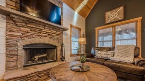 A cozy living room with a stone fireplace, leather sofa, and a round wooden coffee table. - Cozy Dahlonega Cabin w/ Hot Tub. Surrounded by wineries and 8 mins to downtown! (Lumpkin County)