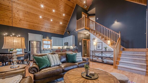 A spacious living area with a leather sofa, a round coffee table, and a staircase leading to an upper level. - Cozy Dahlonega Cabin w/ Hot Tub. Surrounded by wineries and 8 mins to downtown! (Lumpkin County)