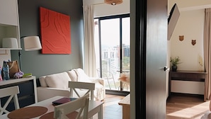 A modern living room with a sofa, a dining table with chairs, a large window with a city view, and a small kitchen area. - Luxury Apartment - Rooftop Pool in Zone 10 High Rise (Ciudad de Guatemala)