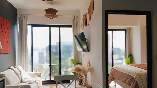 A modern bedroom with a large window, a bed, a desk, and a chair. - Luxury Apartment - Rooftop Pool in Zone 10 High Rise (Ciudad de Guatemala)