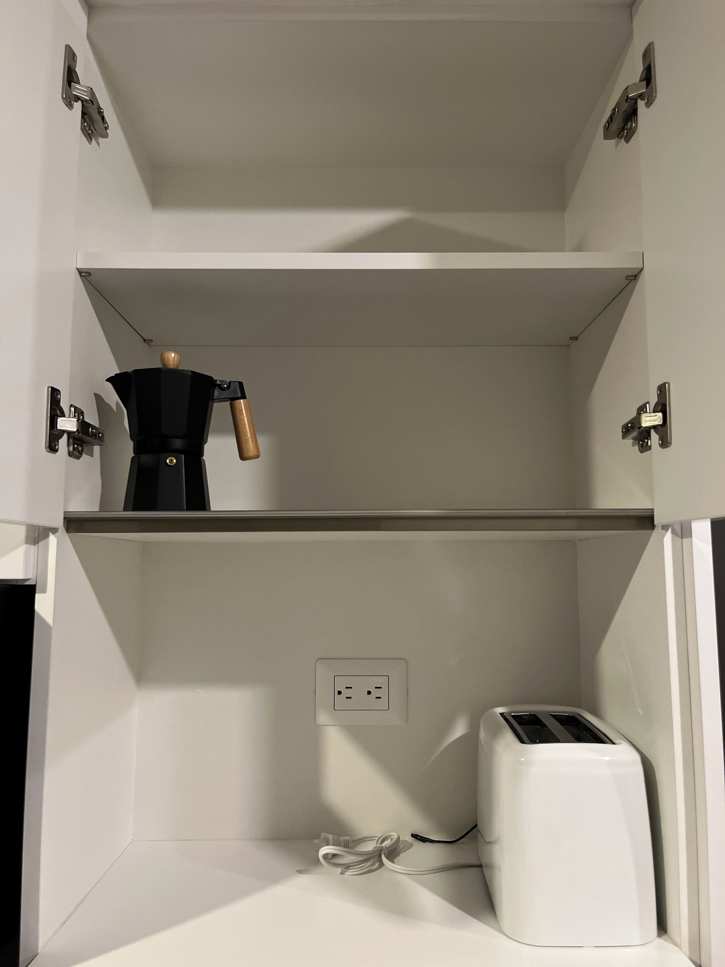 Une cuisine avec une machine à café sur l’étagère supérieure et un grille-pain sur l’étagère inférieure.