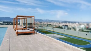 A rooftop pool area with wooden loungers and a view of a cityscape and mountains. - Luxury Apartment - Rooftop Pool in Zone 10 High Rise (Ciudad de Guatemala)