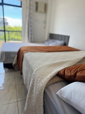A hotel room with two beds, a large window, and a view of greenery outside. - Cozy 2-bedroom apartment in charming Braga Cabo Frio with AC, WiFi (Braga Cabo Frio)