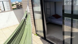 Ein Balkon mit einer Hängematte, eine Glastür zu einem Zimmer mit einem Etagenbett und ein gefliester Boden.