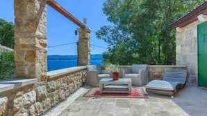 A stone-walled outdoor seating area with wicker furniture and a view of the sea. - Villa Eden - two charming stone houses with sea views by MyWaycation (Omis)