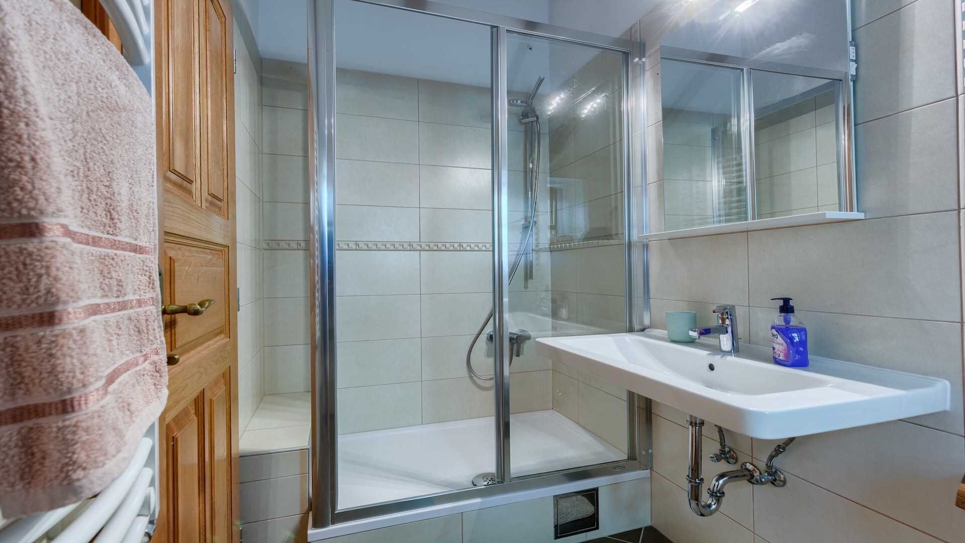 A modern bathroom with a glass shower enclosure, a white sink with a mirror, and a towel rack.