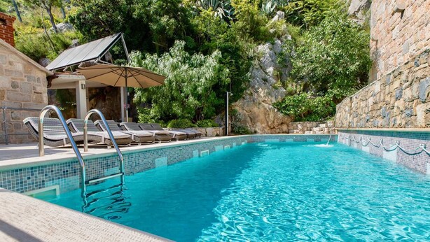 A clear blue pool with a tiled edge, surrounded by lounge chairs and a stone wall. - Villa Eden - two charming stone houses with sea views by MyWaycation (Omis)