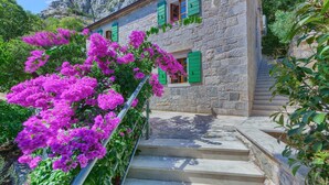 A stone building with green shutters, a staircase, and vibrant pink flowers. - Villa Eden - two charming stone houses with sea views by MyWaycation (Omis)