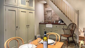 A dining table set with plates, wine glasses, and a bottle of wine in a room with stone walls and a staircase.