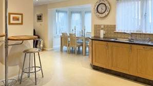 A modern kitchen with wooden cabinets, a dining area with a table and chairs, and a bar stool.