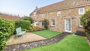 A stone house with a paved driveway, a green lawn, and a bench.