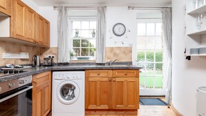 A kitchen with wooden cabinets, a washing machine, a sink, and a clock on the wall.