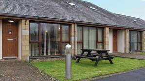 A building with a tiled roof, large windows, and a picnic table in the front.