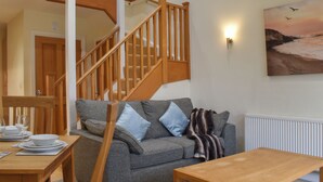 A cozy living room with a grey sofa, wooden coffee table, and a staircase.