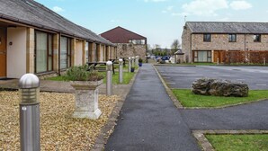 A pathway leading to a row of buildings with a stone facade, a parking area, and a clear sky.