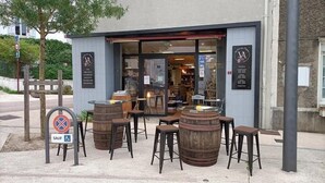 Un petit bar avec des tabourets en bois et des barils, un panneau indiquant qu’il est interdit de se garer, et une devanture avec des vitrines.