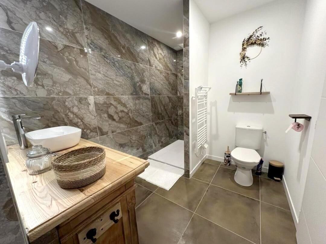 A bathroom with a marble wall, a wooden vanity, a white sink, and a toilet.