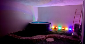 Un jacuzzi en una habitación con borde de piedra y luces de colores.