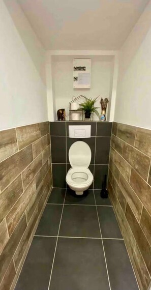 Un baño pequeño con un inodoro, un estante con una planta y un letrero en la pared.