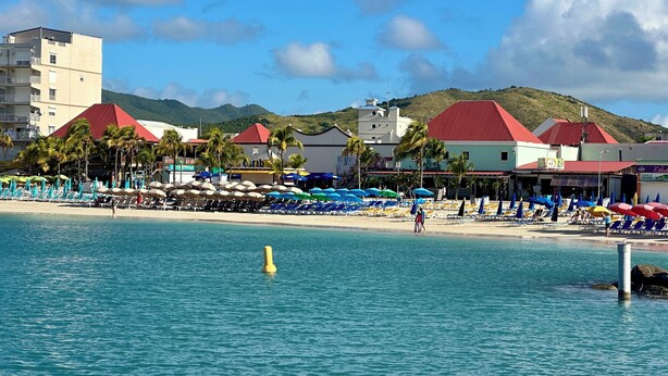 Un hotel frente a la playa con piscina, tumbonas y sombrillas.