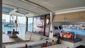 Una pequeña cocina con mostrador, pileta y alacenas. Una ventana ofrece vistas al mar y a los barcos.