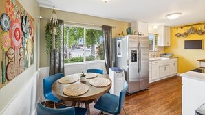 A compact kitchen with a refrigerator, stove, and dining area with blue chairs and a round table. - Garden Sanctuary • Fire Pit • Kitchen & Privacy (San Jose)