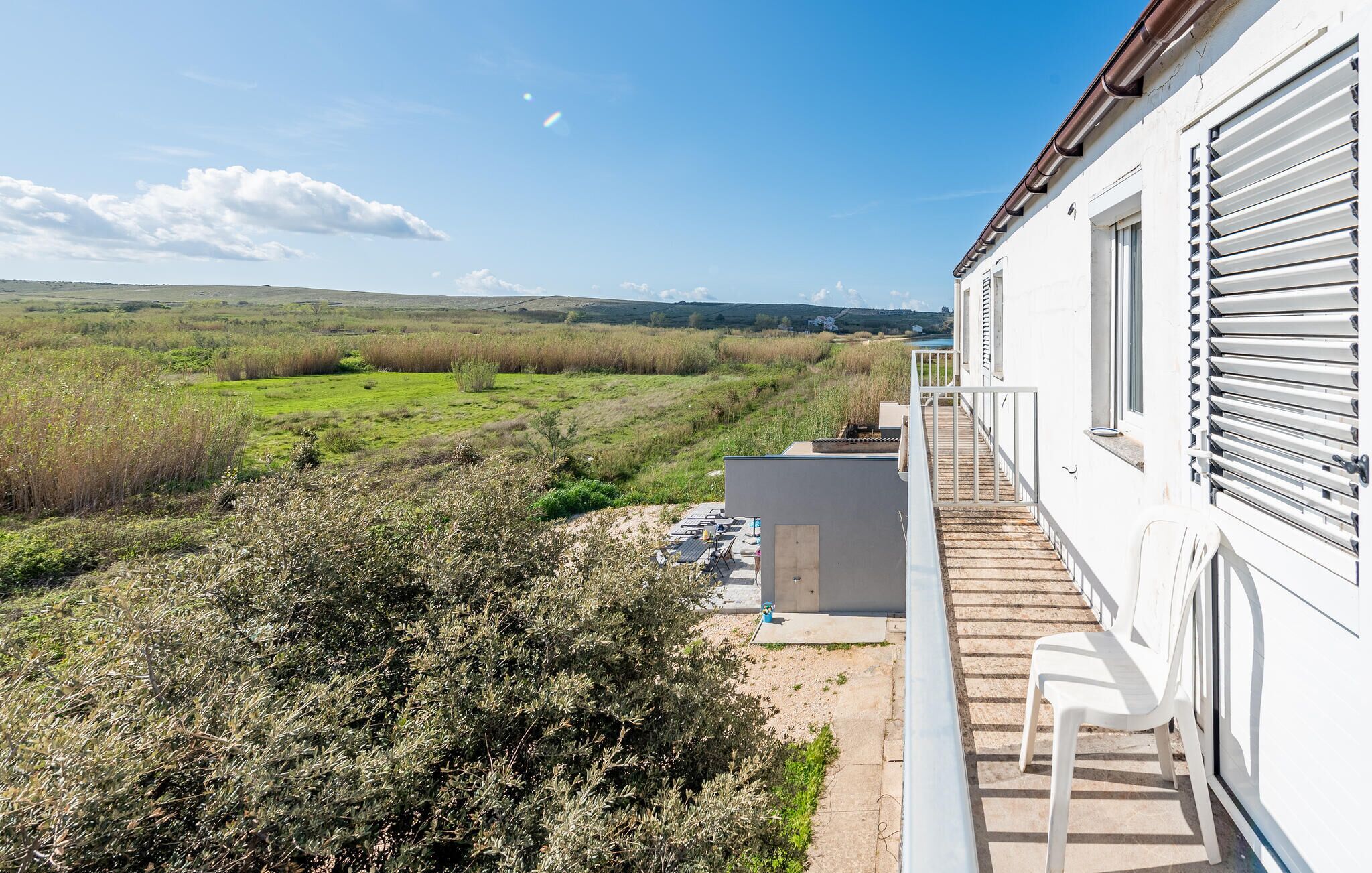 A white building with a balcony overlooking a grassy field and a distant view of hills.