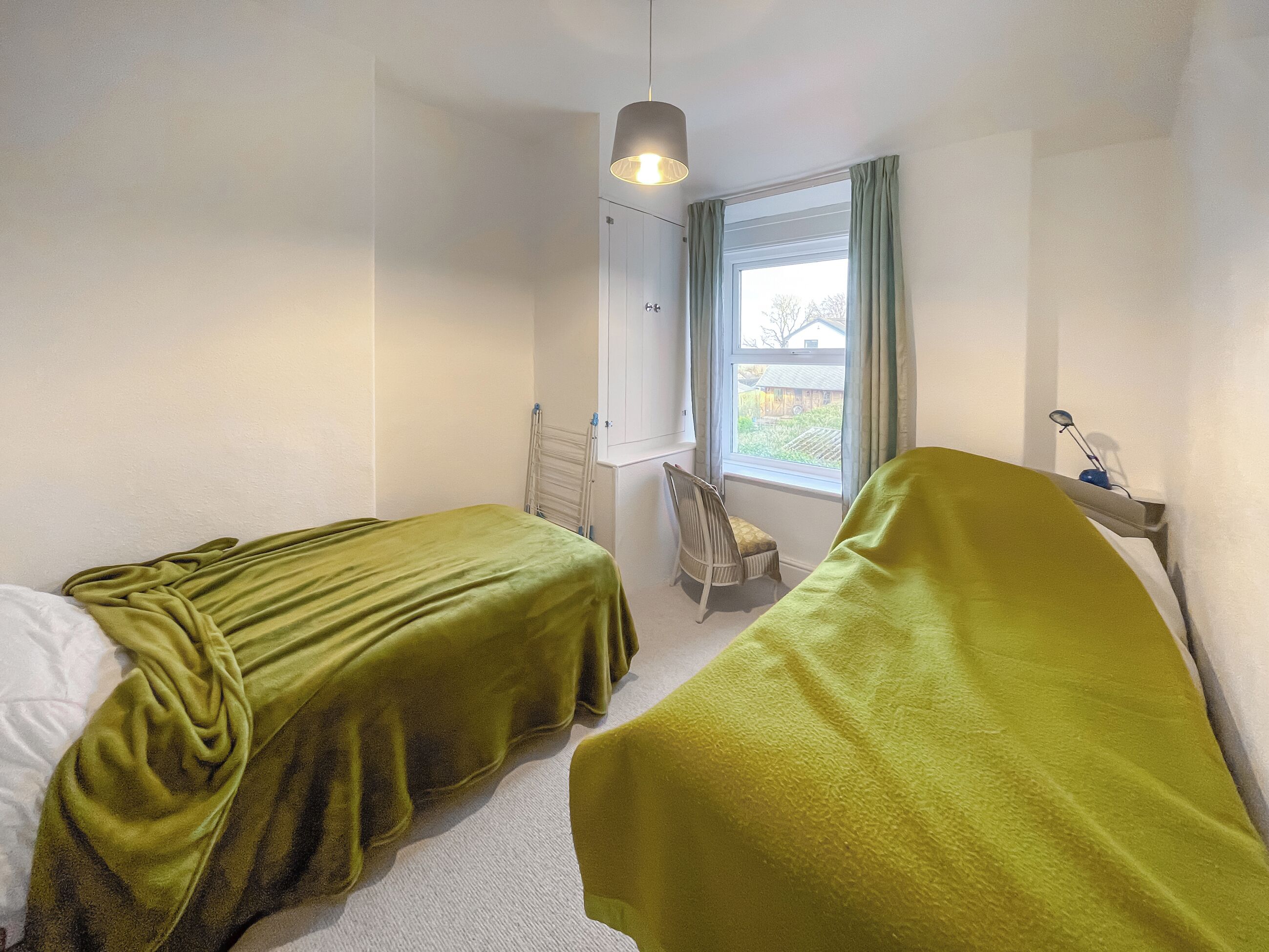 A room with two beds, a window with curtains, a radiator, and a hanging light fixture.