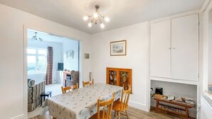 Comedor con una mesa cubierta con mantel, sillas de madera, una araña y un aparador con puertas de cristal.