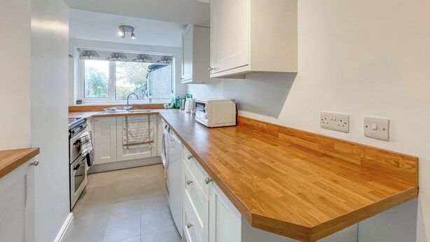 Una cocina con armarios blancos, encimera de madera, horno empotrado, un fregadero y una ventana con vistas al exterior.