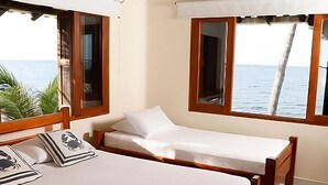 Une chambre avec deux lits, des têtes de lit en bois, du linge de lit blanc et de grandes fenêtres donnant sur la mer.