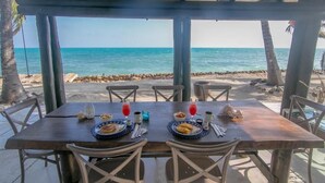 Un espace de restauration en plein air offrant une vue sur l’océan, avec une table en bois mise en place, comprenant des assiettes, des couverts et des boissons.