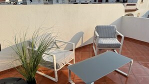 Eine Dachterrasse mit einem weißen Metalltisch und zwei Stühlen, einer gestreift und einer einfarbig.