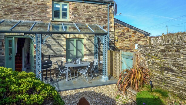 A stone house with a covered patio, outdoor seating, and a dog in the garden. - 2 bedroom accommodation in Mawgan Porth (Mawgan Porth)