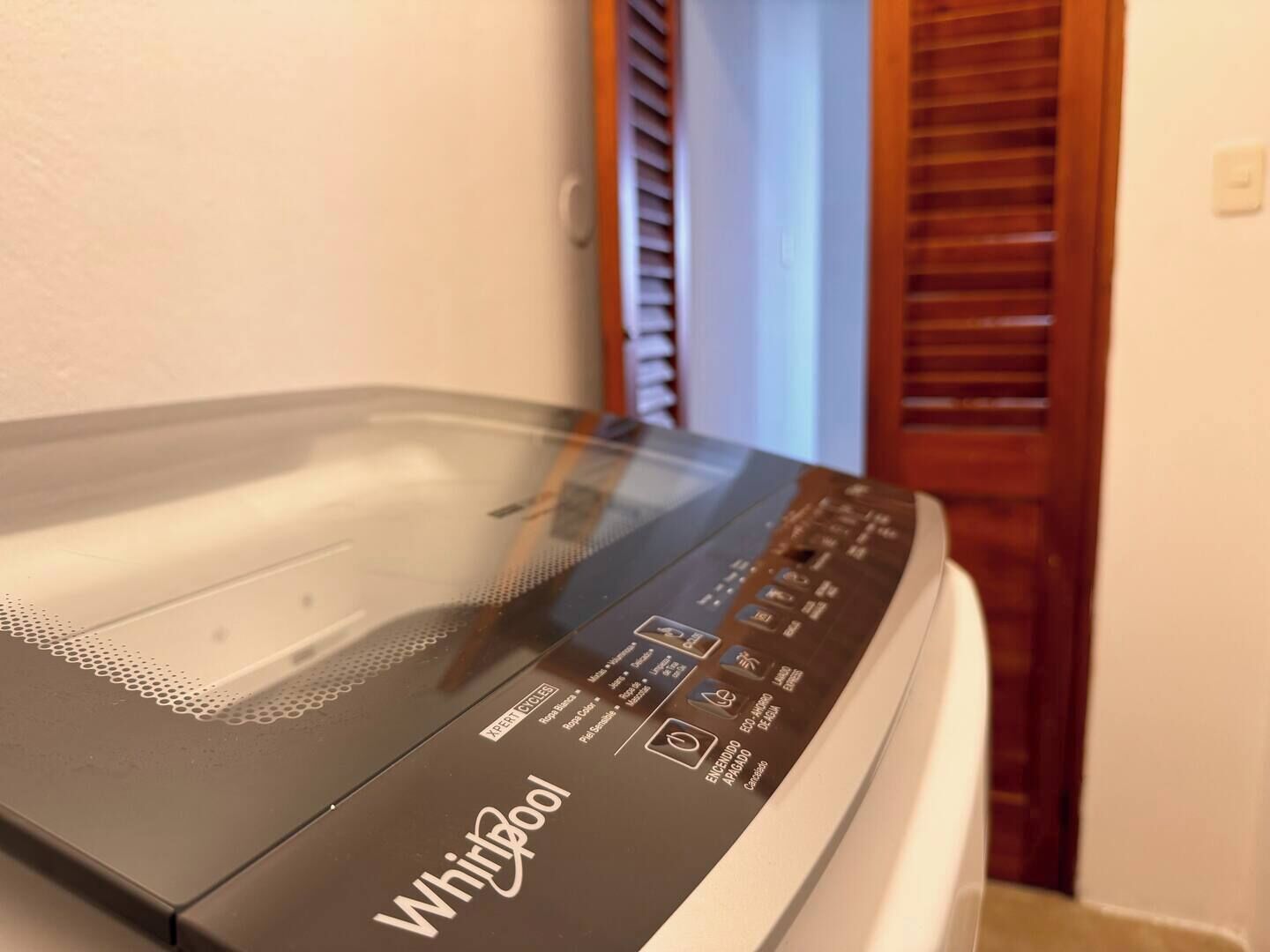 A Whirlpool washing machine in a room with a wooden door and a white wall.