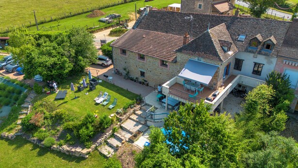 A stone house with a large patio, surrounded by lush greenery and a fenced yard. - La maison de la colline (Vers)