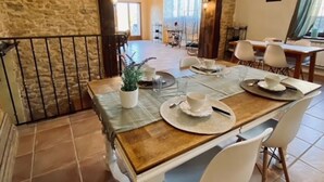 A dining area with a rustic stone wall, a wooden table set for four, and white chairs. - La maison de la colline (Vers)