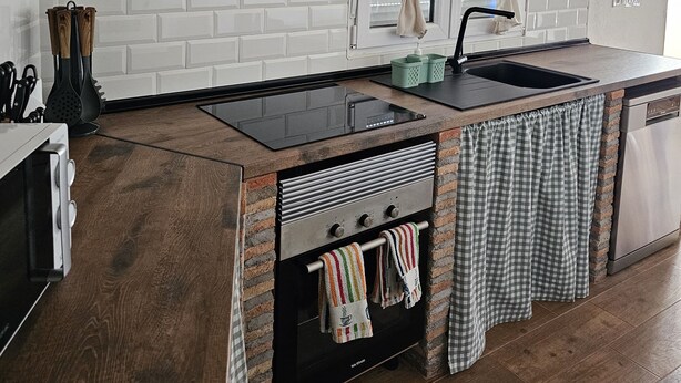 A modern kitchen with a brick backsplash, a black range hood, a built-in oven, a sink, and a dishwasher.