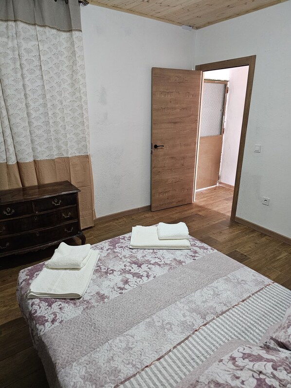 A bedroom with a bed, a wooden dresser, and a door leading to another room. - Casa Rural El Valle (San Bartolomé de las Abiertas)