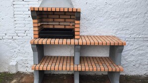 A brick-built outdoor oven with a chimney, set against a white wall.