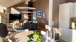 A modern living room with a large TV, multiple seating options, and a dining area.