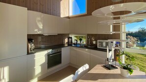 A modern kitchen with wooden cabinets, a built-in oven, and a large window overlooking a garden.