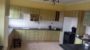 A kitchen with wooden cabinets, a black countertop, a stove, and a small stool. - New California  (Lilongwe)