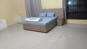 A bedroom with a bed, a nightstand, a wardrobe, and a window with a metal grill. - New California  (Lilongwe)