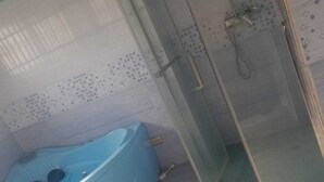 A bathroom with a blue bathtub and a glass-enclosed shower area. - New California  (Lilongwe)