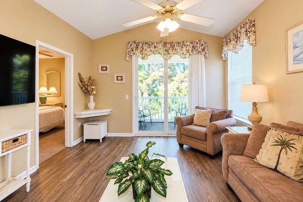 A living room with a ceiling fan, a sofa, a coffee table with a plant, and a television.