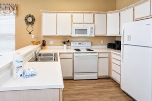 A kitchen with white cabinets, a microwave, a stove, a sink, and a refrigerator.