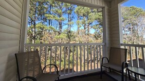 A covered porch with two chairs and a table, overlooking a forested area. - River Oaks Condo + Pools, King Suite, Near Beach (Myrtle Beach)
