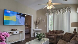 A living room with a television, a ceiling fan, a sofa, and a coffee table. - River Oaks Condo + Pools, King Suite, Near Beach (Myrtle Beach)