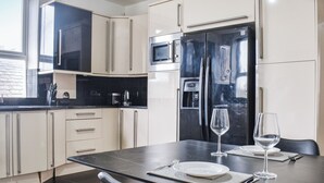 Une cuisine moderne avec des meubles blancs, un plan de travail noir et un coin repas composé d’une table, de chaises et de verres à vin.